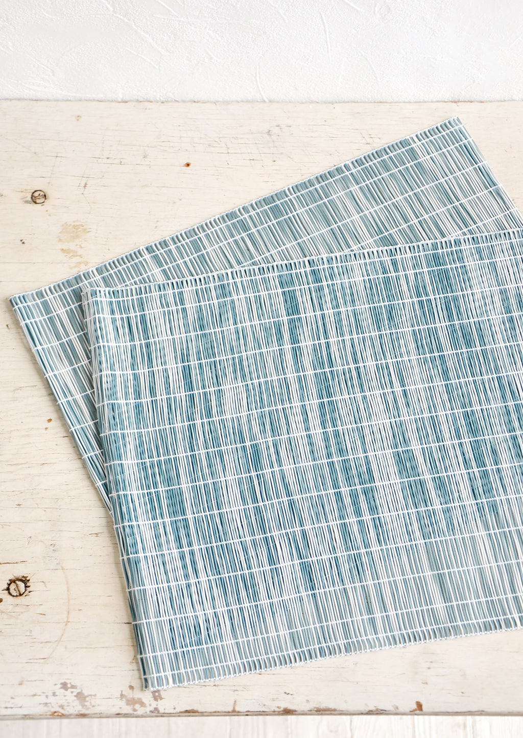 Teal: A pair of placemats made from intertwined, vertically woven vinyl in teal and white.