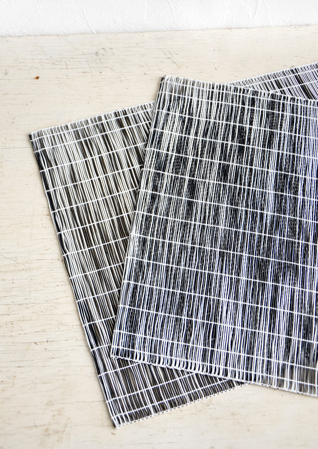 Black: A pair of placemats made from intertwined, vertically woven vinyl in black and white.