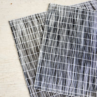 Black: A pair of placemats made from intertwined, vertically woven vinyl in black and white.