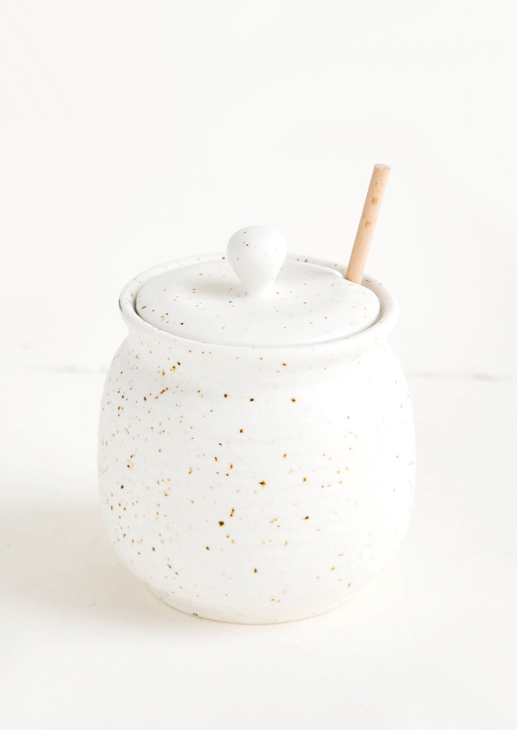 1: Round ceramic honey jar in speckled white glaze with fixed slot in lid for dipper