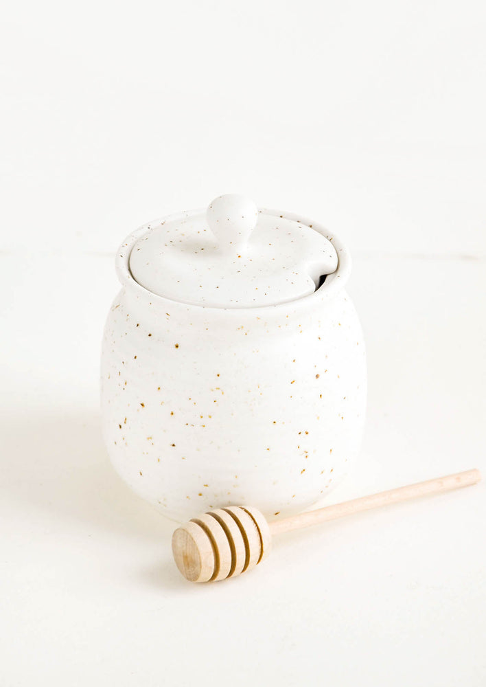Round ceramic honey jar in speckled white glaze with lid and wooden dipper 