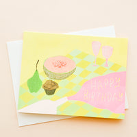 1: Greeting card with picnic setting, spilled wine puddle has letters reading "Happy Birthday"