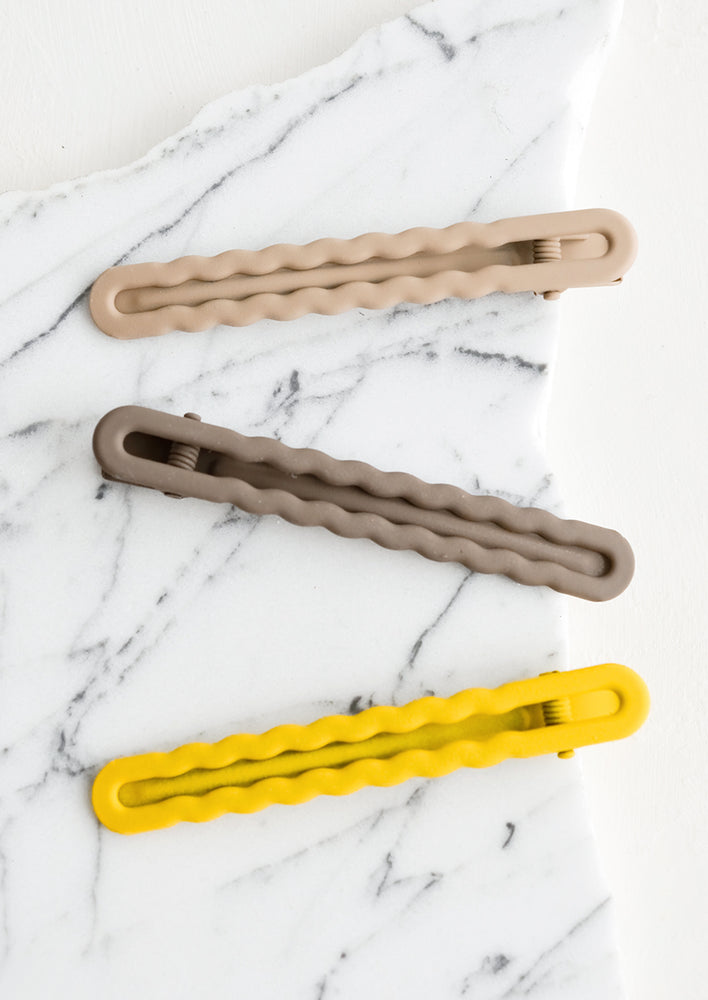 Three hair clips with wavy squiggle design in gradient yellow and grey hues.