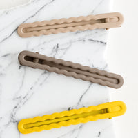 Yellow Multi: Three hair clips with wavy squiggle design in gradient yellow and grey hues.