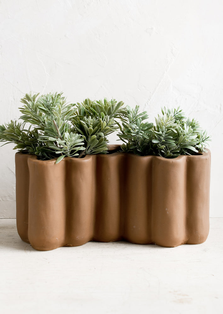 A brown ceramic planter in squiggle shape, with plant inside.