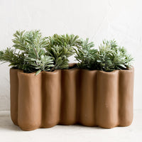 1: A brown ceramic planter in squiggle shape, with plant inside.