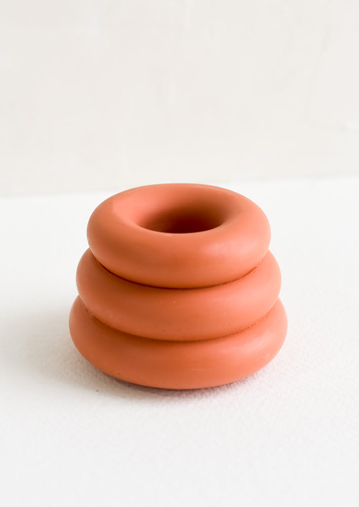 A taper candle holder with 3-layer stacked donut shape in terracotta.