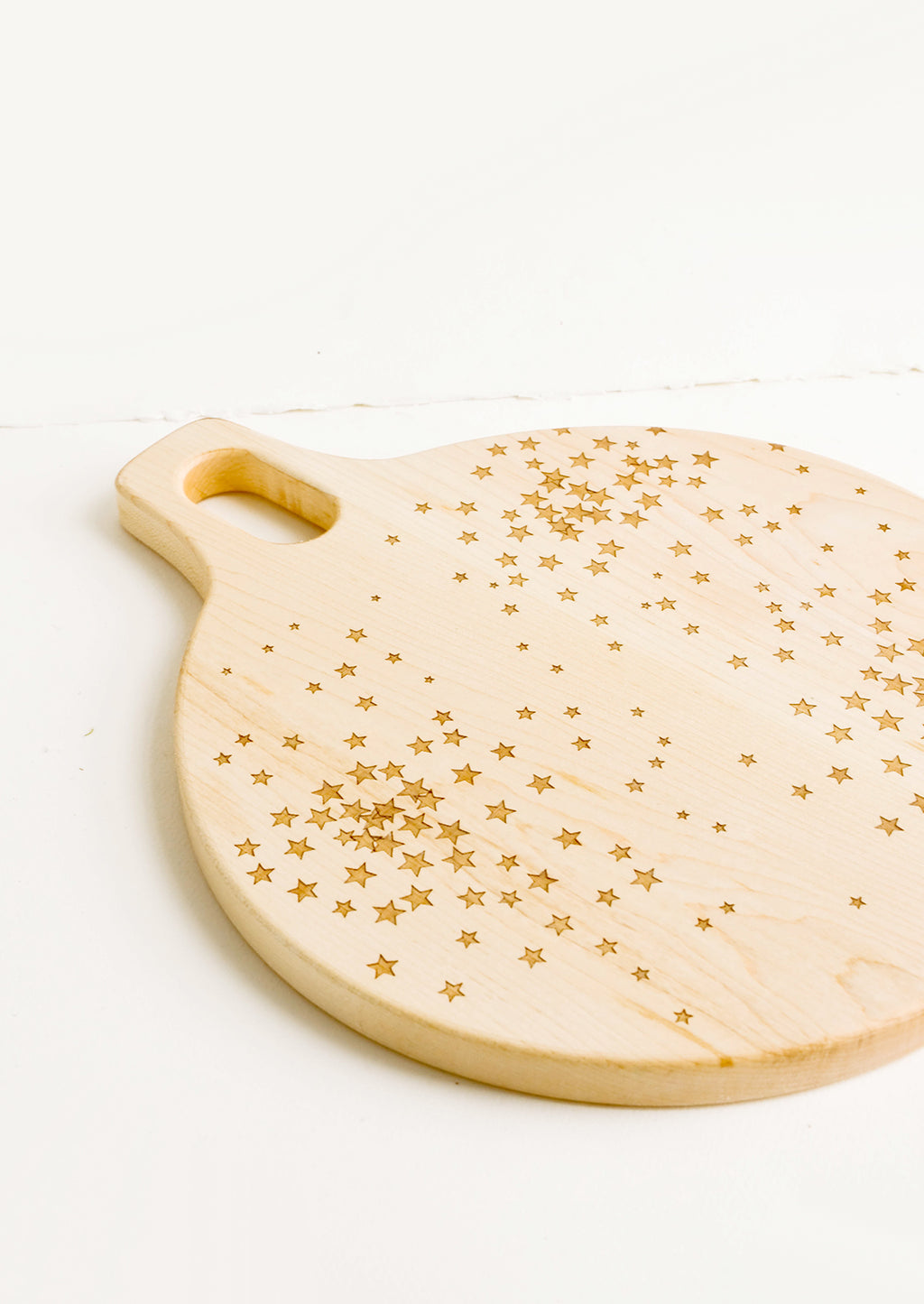 2: Round paddle-style cutting board in maple wood with scattered star pattern