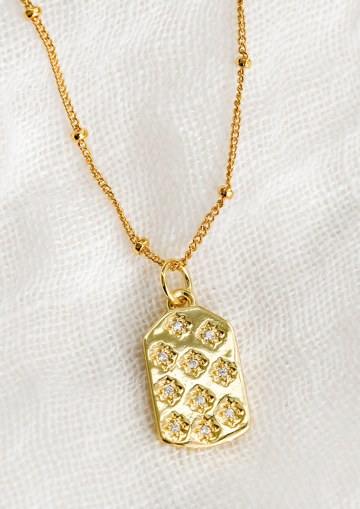 A gold tag charm necklace with crystal pave star detailing.