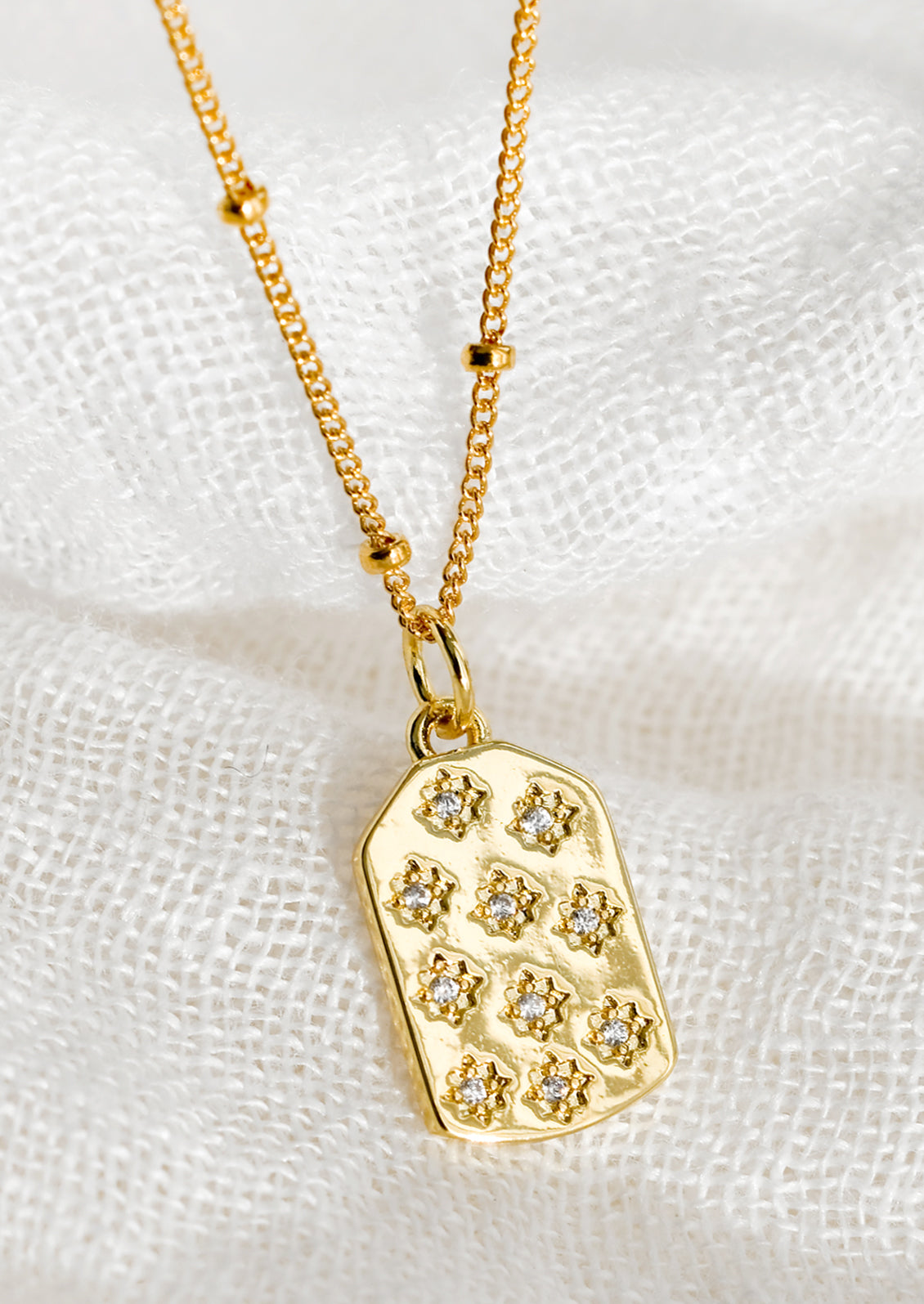 A gold tag charm necklace with crystal pave star detailing.