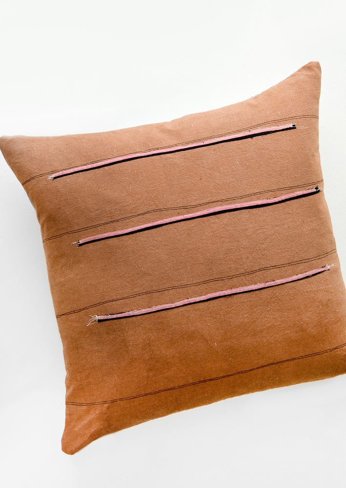 Throw pillow in reddish brown fabric with thin black stripes and sewn-on pink and black stripes