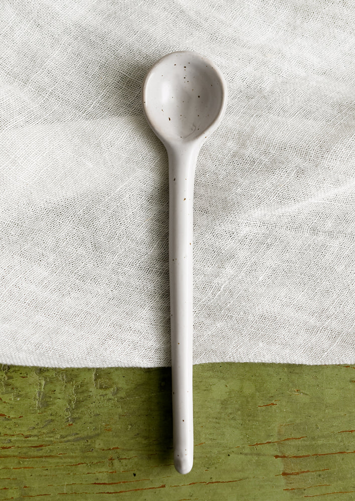 A stoneware spoon in white with dark speckles.