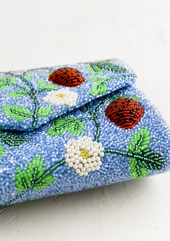 3: A blue beaded clutch with red strawberry pattern.