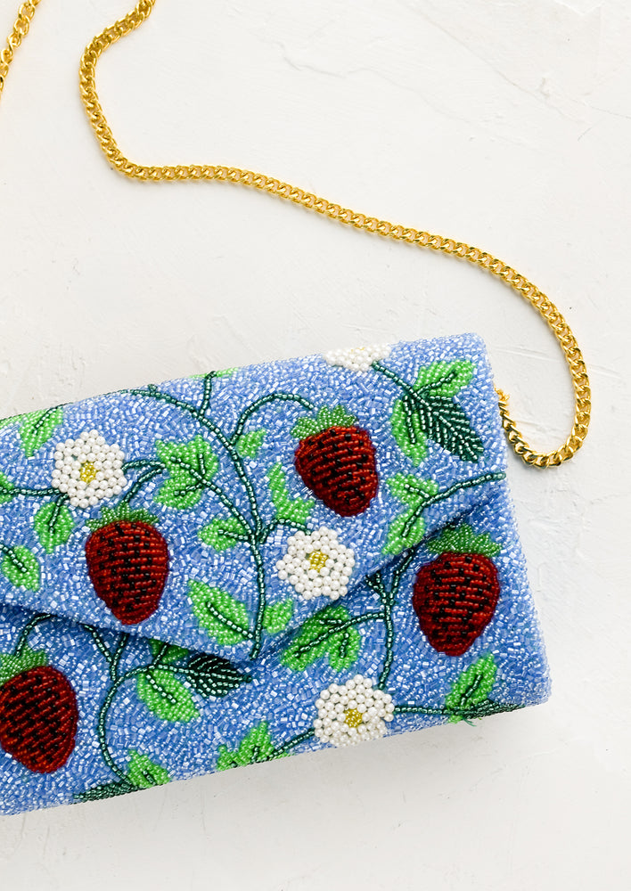 A blue beaded clutch with red strawberry pattern and gold chain strap.