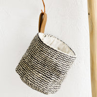 1: A black and white striped jute hanging basket with faux leather strap.