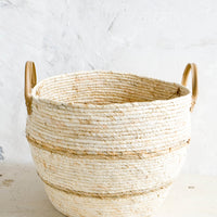 Large [$54.99]: Round storage basket woven from natural maize fiber with tan stripes and leather handles at sides