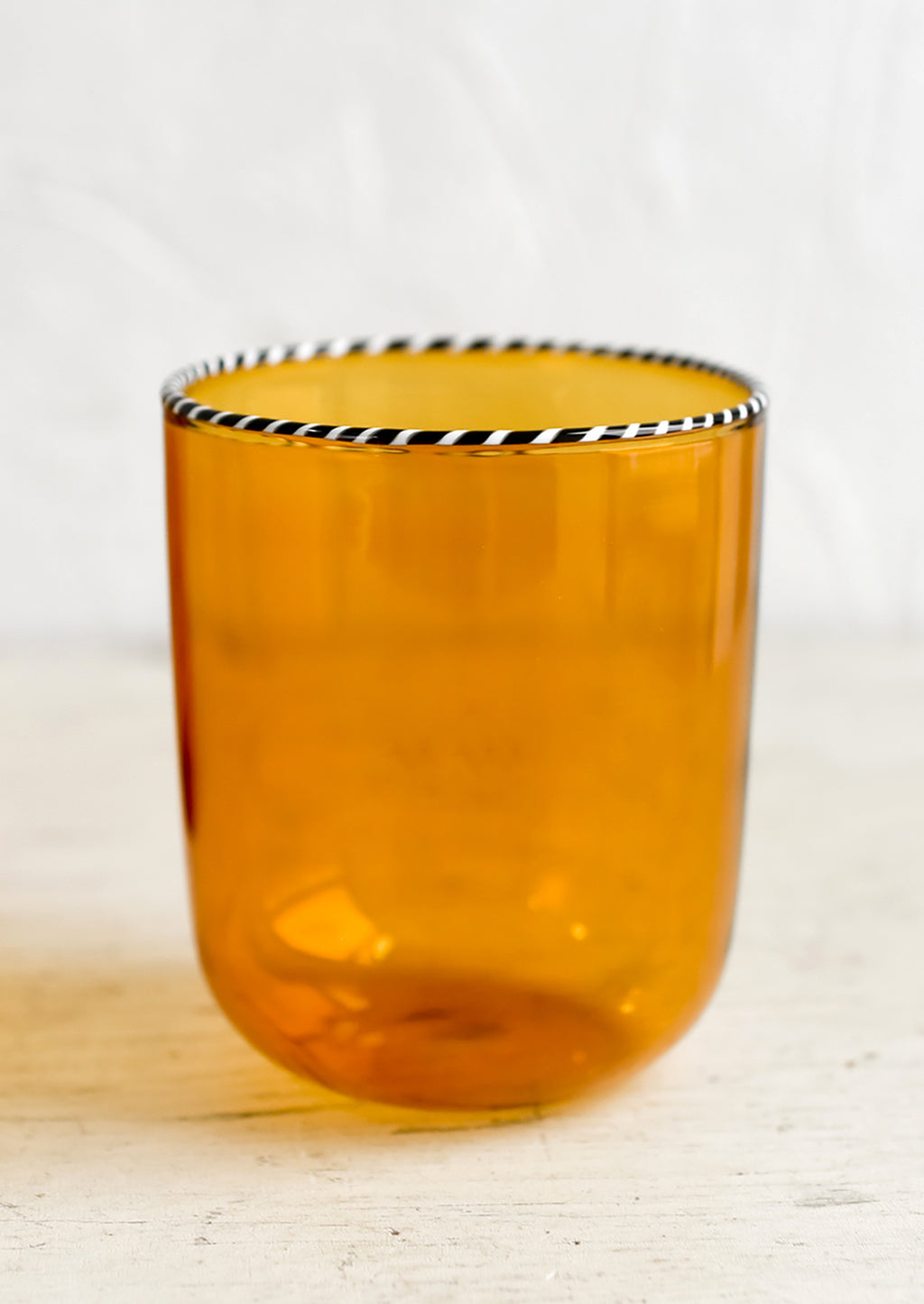Amber: A transparent glass tumbler in amber color with black and white striped rim.
