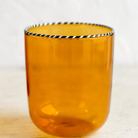 Amber: A transparent glass tumbler in amber color with black and white striped rim.