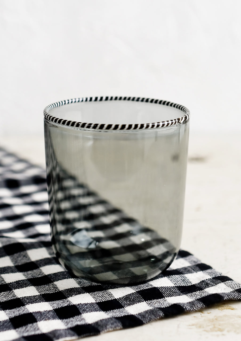 Smoke: A transparent glass tumbler in grey color with black and white striped rim.