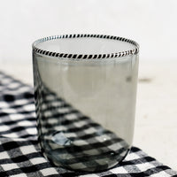 Smoke: A transparent glass tumbler in grey color with black and white striped rim.