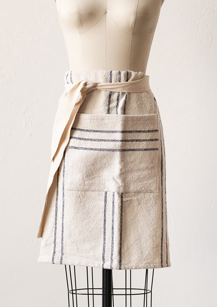 A half apron in ivory with black stripes and front pocket.