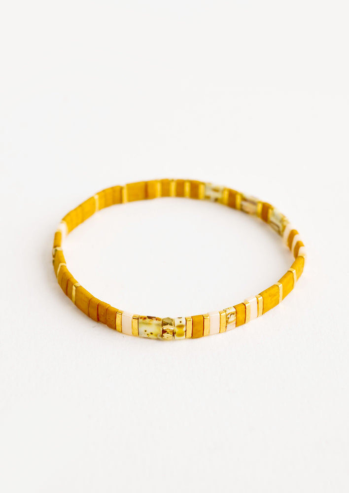Bracelet featuring flat mustard beads interspersed with flat gold bead on an elastic cord.
