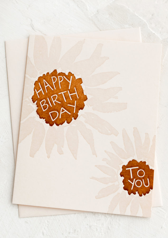 A pink greeting card with pale sunflower design, reading "Happy Birthday", "To You", in the flowers.