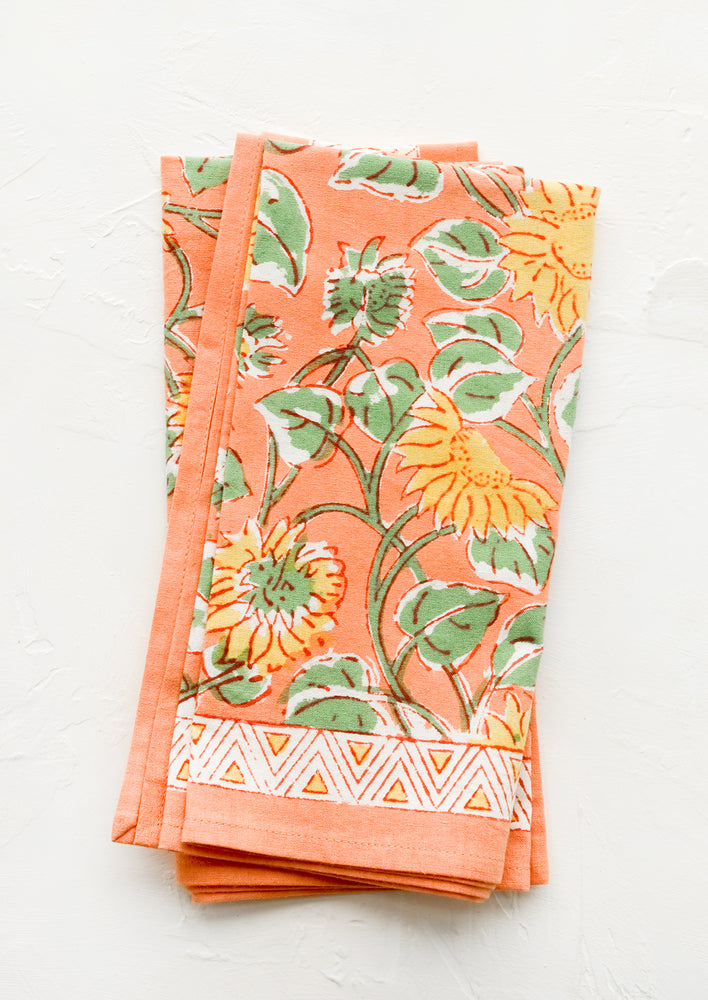 Pair of peach cotton napkins with yellow and green sunflower print.
