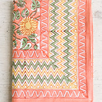 1: A block printed tablecloth in peach, mint and yellow sunflower pattern with zigzag border.