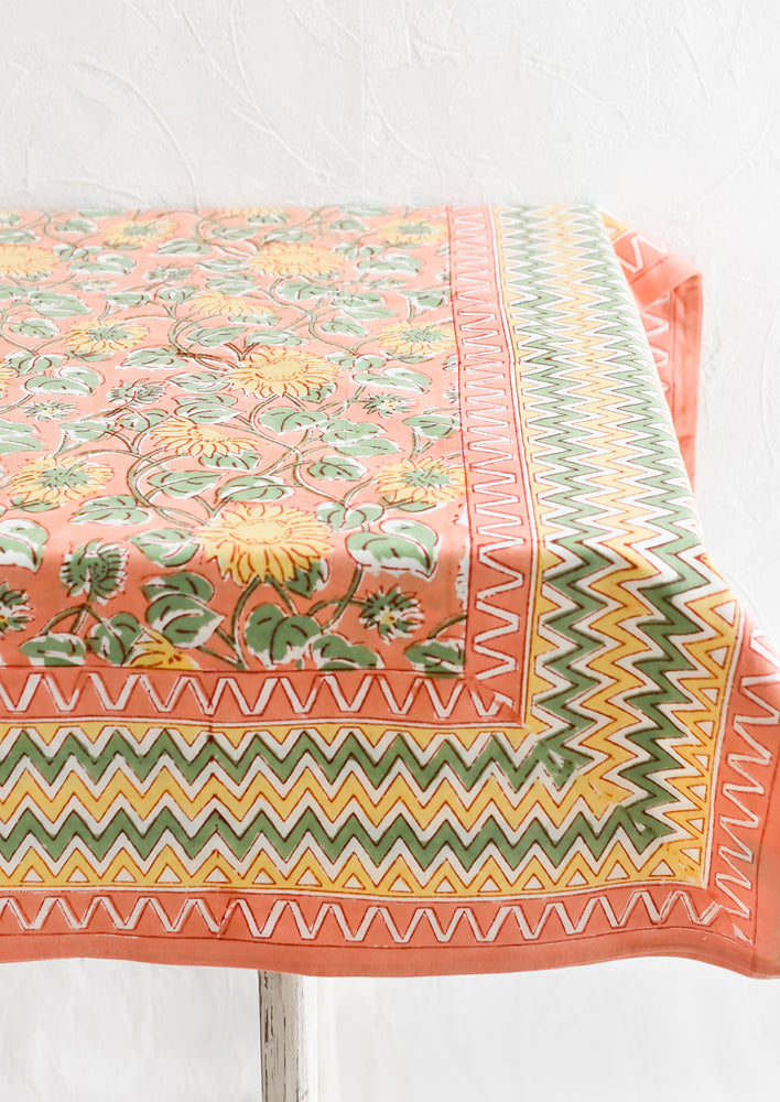2: A block printed tablecloth in peach, mint and yellow sunflower pattern with zigzag border.