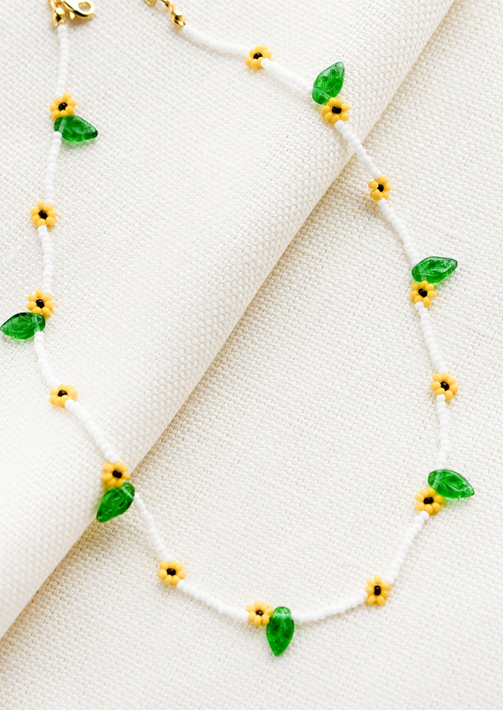 A white beaded necklace with yellow "sunflowers" and green glass leaf beads.
