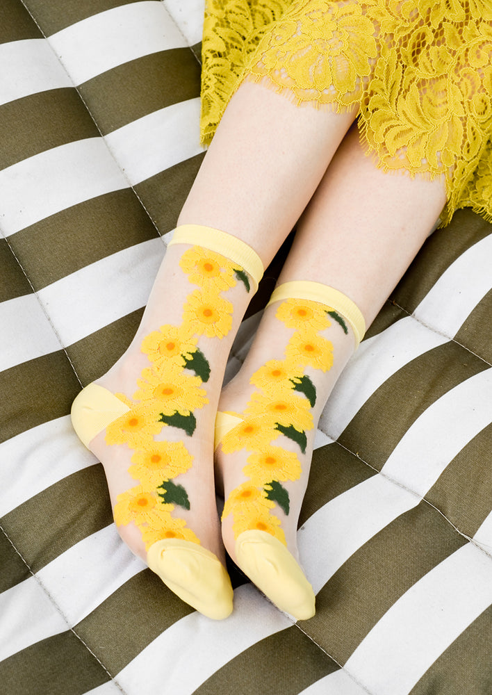 3: A woman's ankles on a hammock wearing sheer sunflower socks with yellow lace skirt.