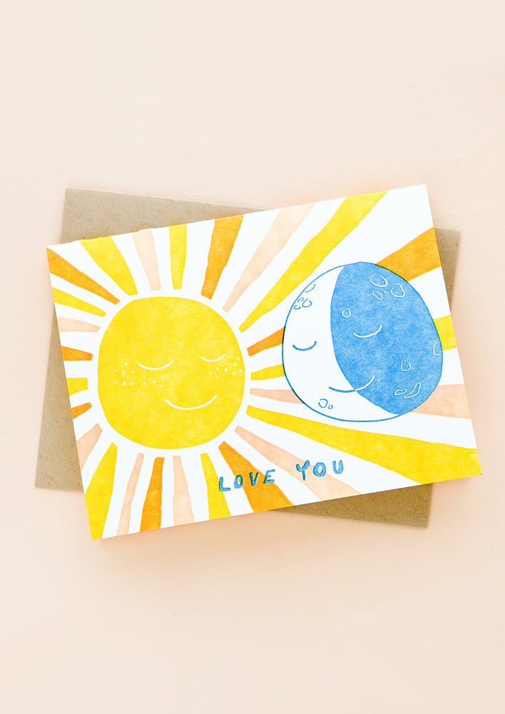A greeting card and kraft envelope. Card features image of sun and moon with text beneath reading "Love you"
