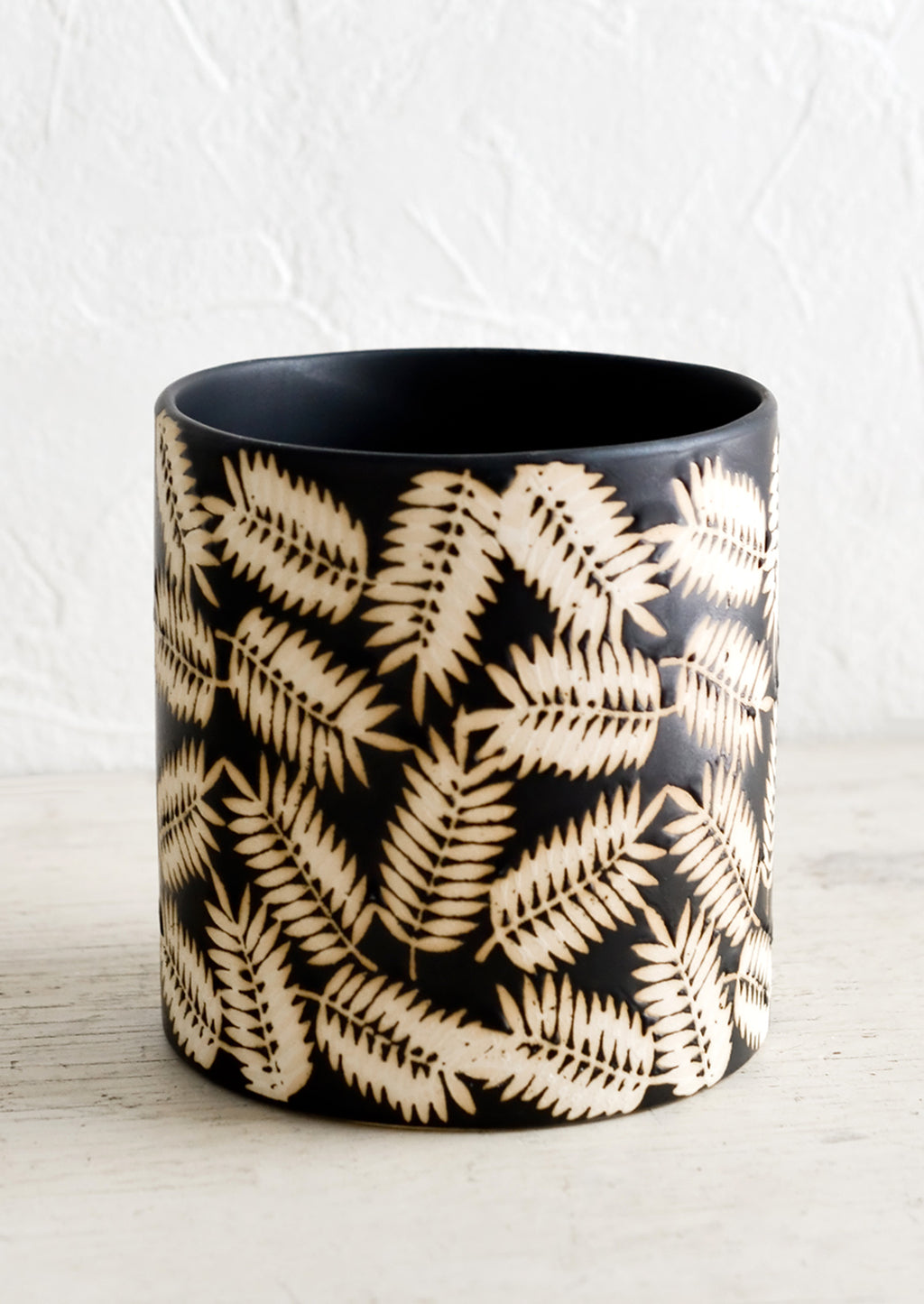 1: A round black ceramic planter with resist print of palm leaves.