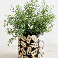 2: A ceramic planter with palm leaf print, housing green plant.
