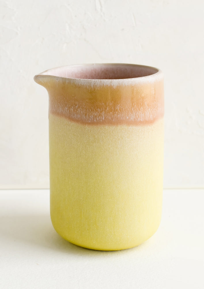 A ceramic pitcher in yellow with pink rim.