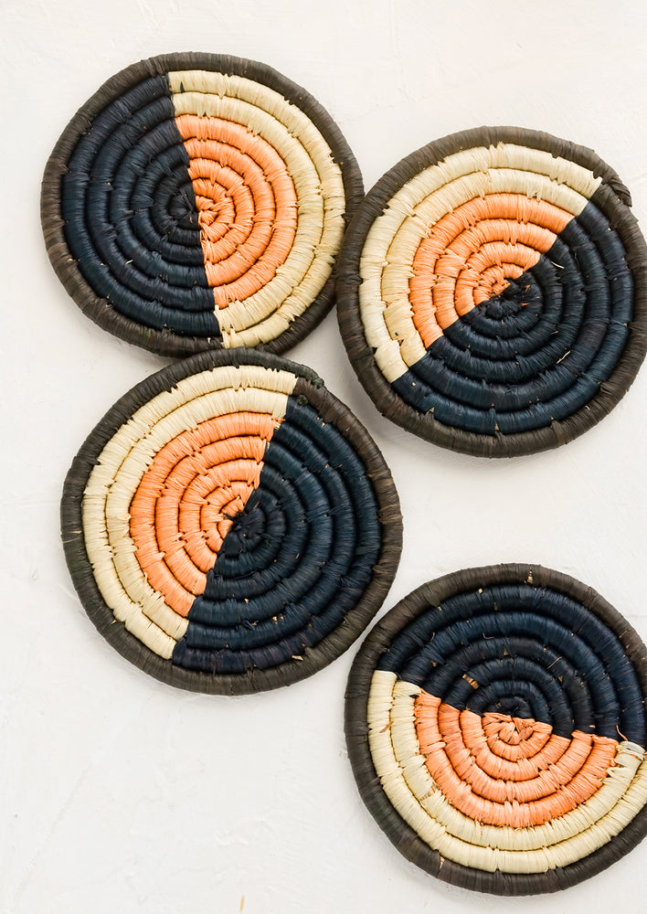 Four round woven raffia coasters in colorblock design.