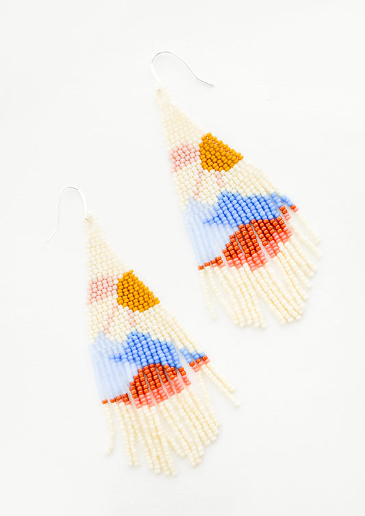 Cream colored beaded fringe earrings with beads of red, blue, pink, and yellow depicting an abstract sun over mountains. 