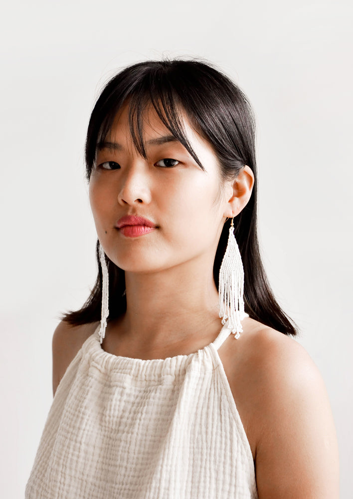 Model wears white beaded fringe earrings and white blouse.