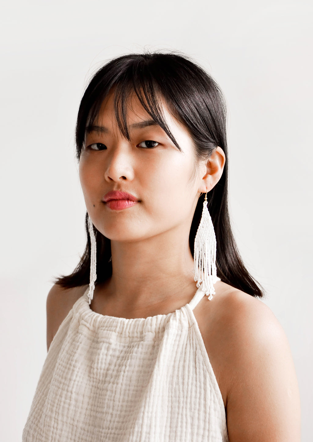 3: Model wears white beaded fringe earrings and white blouse.