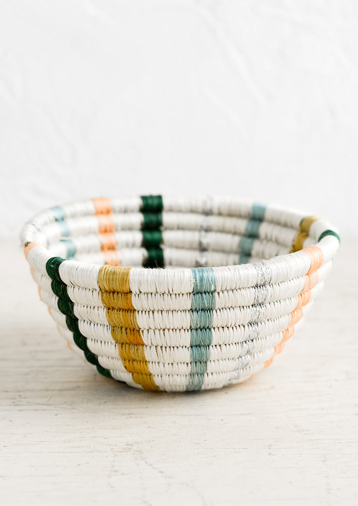 A small woven catchall bowl made from sweetgrass in white with vertical pastel lines.