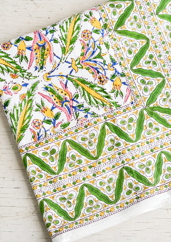 A block printed cotton tablecloth in vibrant green, pink and yellow floral pattern.