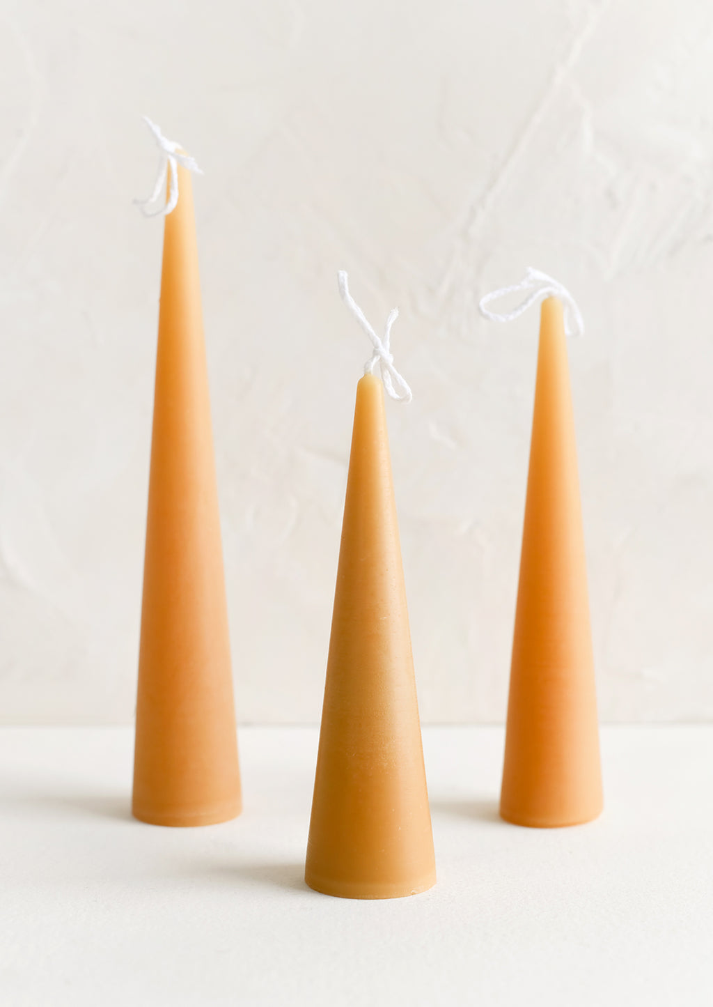 Small / Warm Sand: Three lit cone-shaped taper candles in warm sand.