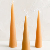 Small / Warm Sand: Three lit cone-shaped taper candles in warm sand.