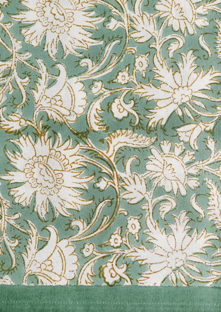 A block print tablecloth in sea green with white and brown floral print.