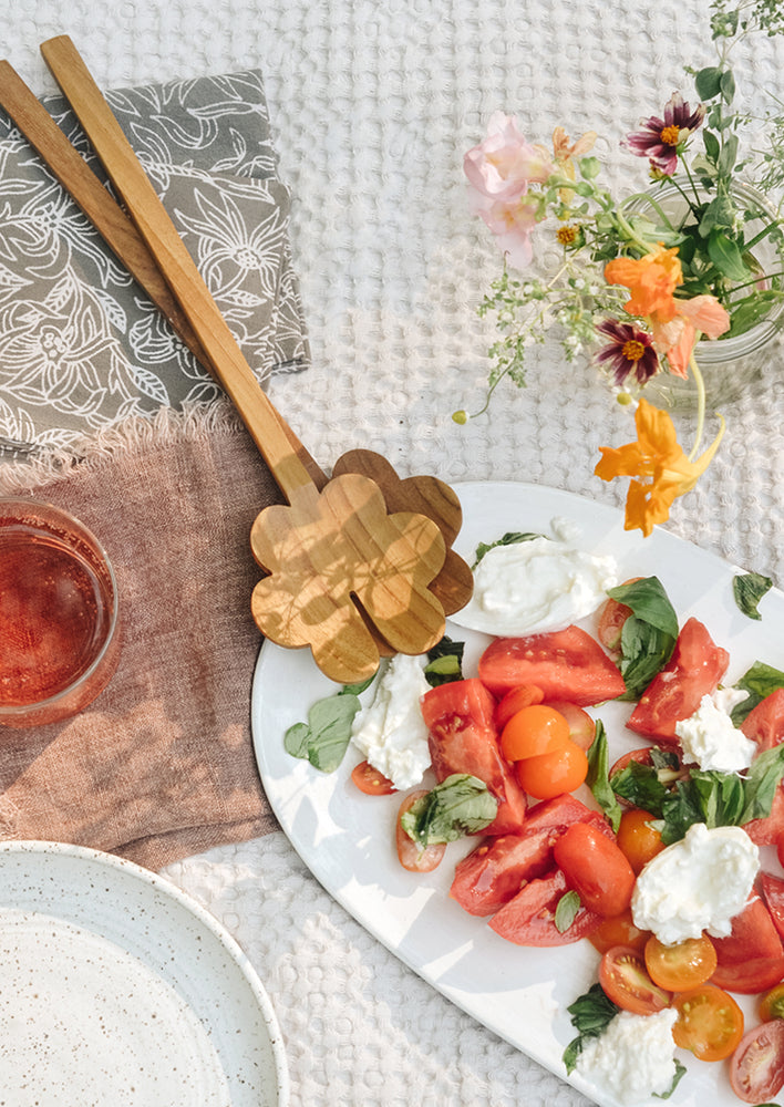 A picnic scene with tomato salad and wooden serving set.