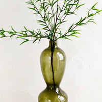 2: A tall glass vase in hourglass silhouette with leafy branches.