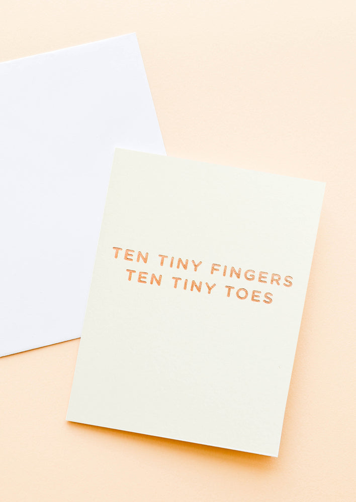 A pale yellow greeting card with gold foil text reading "ten tiny fingers ten tiny toes."