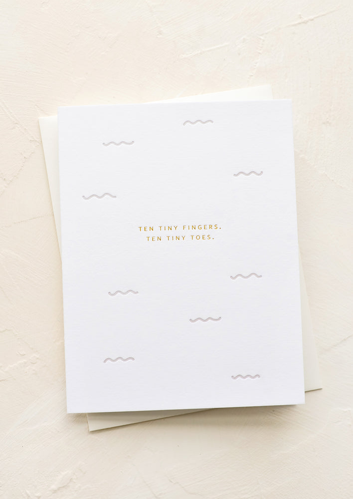 A greeting card with small gold letters reading "Ten tiny fingers, ten tiny toes".