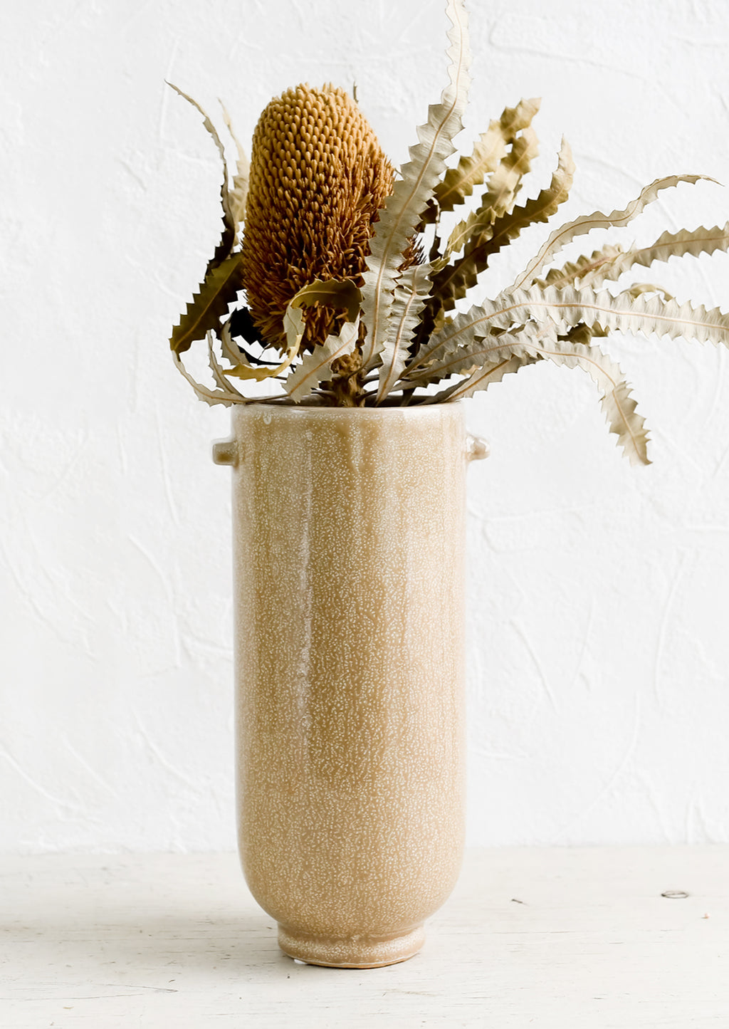 2: A tall brown ceramic vase with dried protea flower.